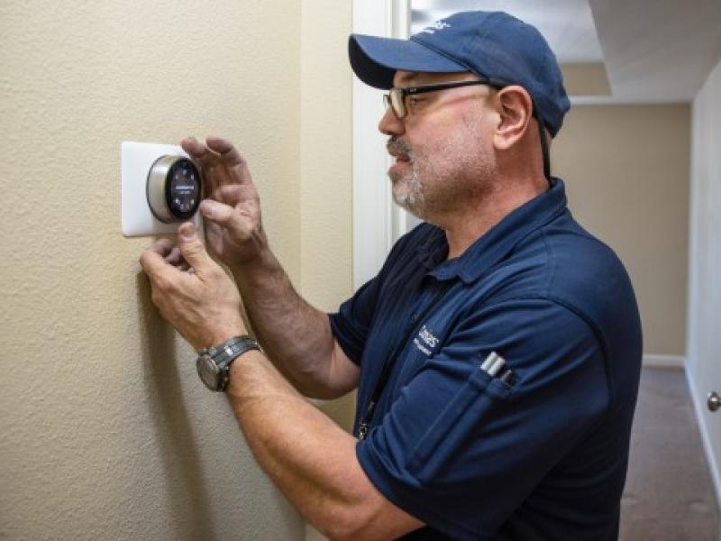 maintenance man improving energy efficiency adjusting nest thermostat